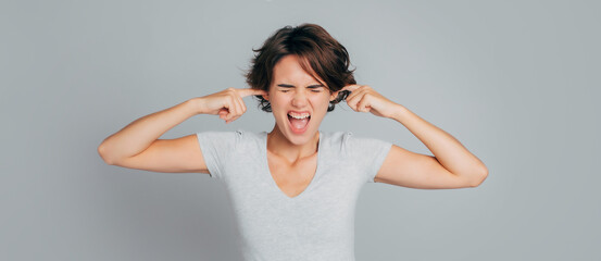 Portrait of young woman covering her ears plugging with fingers and screaming and closed eyes in...