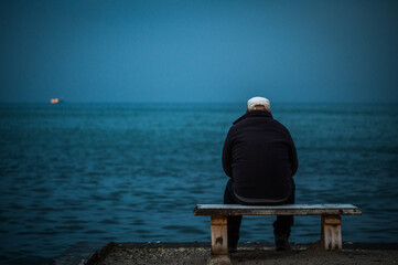 The Old man and the sea - lonely person sitting on a bench looking at the stormy sea