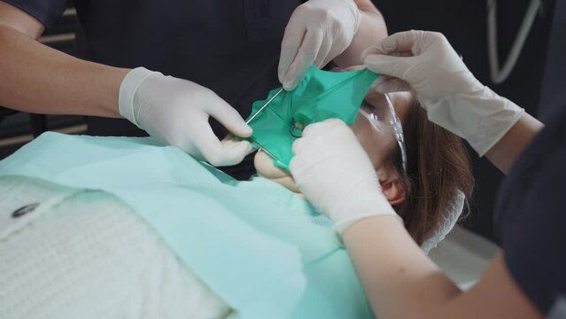 Two unrecognizable medical workers in white sterile gloves putting rubber dam on patient mouth for dental treatment. Teeth. Medical concept