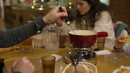 People eating cheese fondue at restaurant, closeup hand dips piece of bread into melted cheese at...
