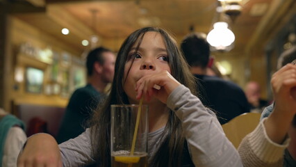 Pensive Little Girl Drinking Ice Tea with Straw at Restaurant in the Evening - Thoughtful Child...