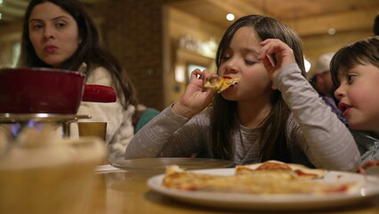 Small girl eating slice of pizza at restaurant, family enjoying time together during weekend activity at evening diner