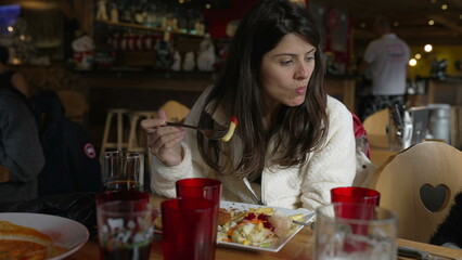 Woman eating at restaurant, candid authentic person in 30s eats fries with fork at diner - interacting with family members off-camera