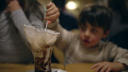 Young boy eating ice cream sundae at restaurant. Child enjoying sugar treat indulgence dessert