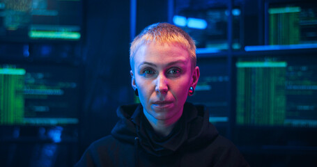 Portrait of Caucasian woman hacker with short hair sitting at night in front of computer. Cyber policewoman turning face to camera and biting cookie. Close up female eating sweets in monitoring room.