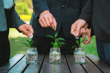 Business people put coin to money saving glass jar on outdoor table as sustainable money growth...