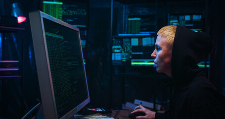 Side view on Caucasian woman with short blond hair and in hood working in cyber security center and...