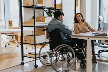 Fototapeta na wymiar Successful woman discussing work with her handicapped male colleague in wheelchair at modern creative office.