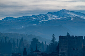 View of the towers of the Alhambra on a misty winter dawn with the snow-capped peaks of the Sierra Nevada in the background