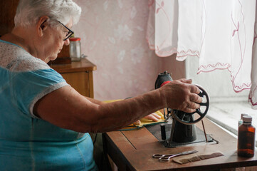 senior woman sewing her cloth with old sewing machine