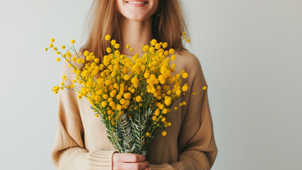 womans day mimosa. young woman holding yellow heart shaped mimosa flowers bouquet on grey background - obrazy, fototapety, plakaty