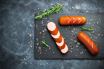 Grill pork sausages on a black stone slate serving board, isolated on a dark background.