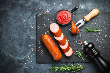 Grill pork sausages on a black stone slate serving board, isolated on a dark background.