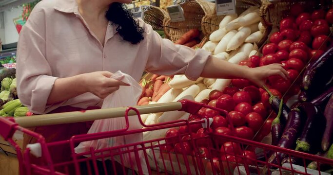 Pretty young beautiful brunette hair woman buys food, tomatoes in the market, in the supermarket. Girl chooses products,vegetables, fruits in the store. Shopping,Vegan sales concept.