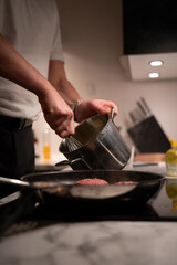 Burger paddies of high quality groundbeef searing on hot pan. Man in white shirt preparing homemade meal. authentic look.