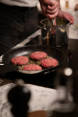 Burger paddies of high quality groundbeef searing on hot pan. Man in white shirt preparing homemade meal. authentic look.
