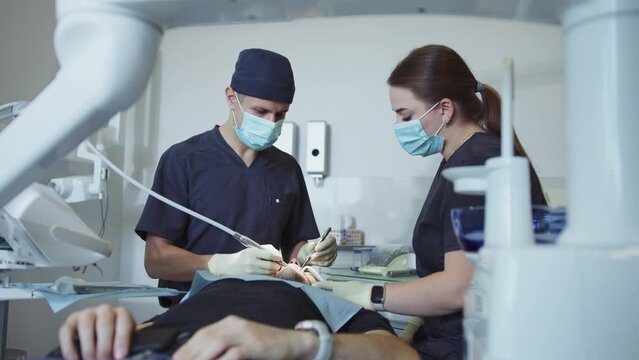 Woman assistants and man dentist in medical masks hold a dental instrument that treats teeth. Hydience and healthy