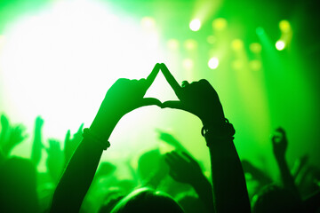 Triangle hands, neon and person in concert audience for music, festival or performance on stage. Party, psychedelic and green light with crowd of people outdoor for event, disco or club celebration