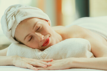 A beautiful young woman lies on a spa bed, her body relaxed and at peace. Pretty caucasian girl surrounded by the spa environment and the gentle aroma of essential oils. Close up. Tranquility.