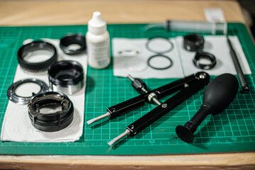 bunch of disassembled camera lens and lens repairing tools equipment laying on green service table waiting for fix and cleaning