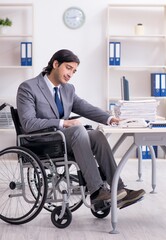 Young handsome employee in wheelchair working in the office