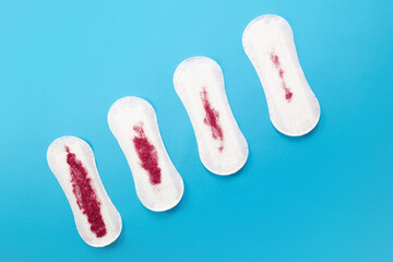 Feminine hygiene pads with red glitter on blue background. First menstrual period concept 