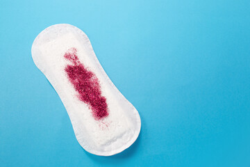 Feminine hygiene pad with red glitter on blue background. First menstrual period concept 