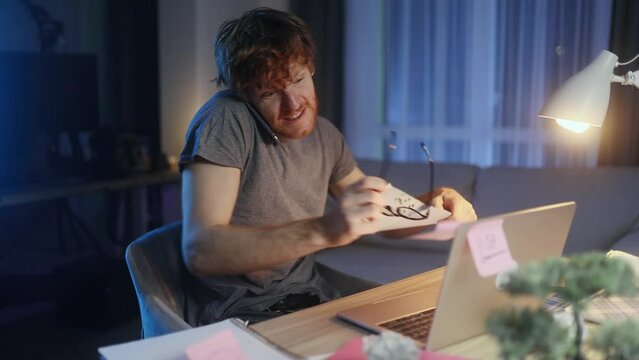 Nervous stressed young man freelancer typing quickly on laptop hurry up scream and warning about deadline while having paper and computer work at late night at home workplace
