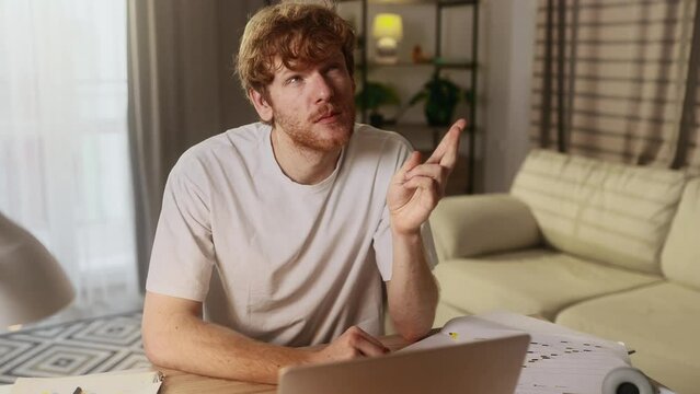 Handsome red haired man student or freelancer thinks questioningly and finding solution with laptop computer at home Idea concept
