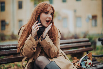 Obraz premium A shocked young woman is having a phone conversation outdoors.