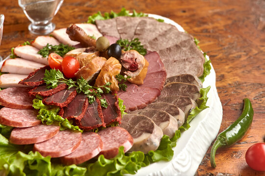 Plate with cold cuts with choice - salami, pieces of sliced ham, sausage, chicken, qazi horse meat, tomatoes on salad, close-up, shallow depth of field