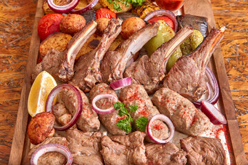Part of the wooden board with fried meat and vegetables on the wooden table, close-up, shallow depth of field. Lamb meat and onion in focus