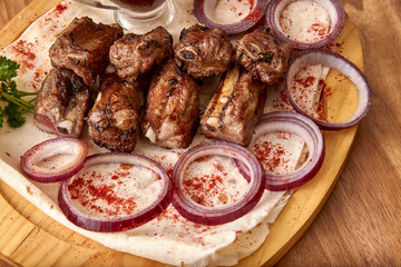 Fried mutton ribs meat with red onion rings, sauce and pita bread on the wooden board on the wooden table. Close-up perspective view, shallow depth of field. Meat and onion in focus