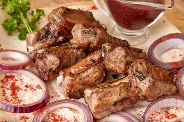 Fried mutton ribs meat with red onion rings, sauce and pita bread on the wooden board on the wooden table. Close-up perspective view, shallow depth of field. Meat and onion in focus