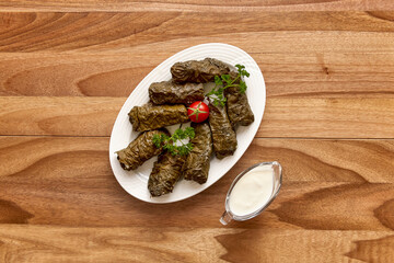 White plate with dolma (meat in grape leaves) on the wooden table with sour cream near it. Top view, flat lay