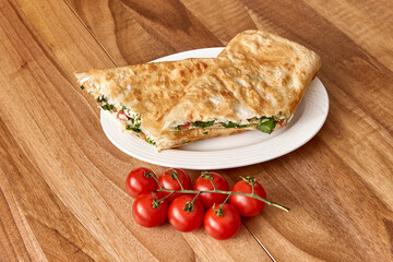 White plate with fried pita roll with salad with greens and tomatoes on the wooden table with cherry tomatoes near it