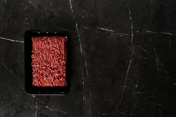 Raw and Fresh Minced Beef in Black Plastic Container just from the store, opened. On dark marble background. Minimalistic food photo, low-key. Top view, copy space - Powered by Adobe