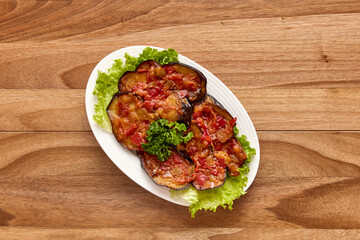 White plate with fried eggplant with tomato sauce on a lettuce leaf on the wooden table. Top view, flat lay
