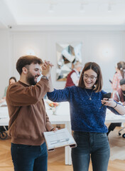 Two joyful coworkers share a high five in a bustling office space, marking a successful moment. Their smiling faces and energetic gesture exude a positive working atmosphere amidst focused colleagues.