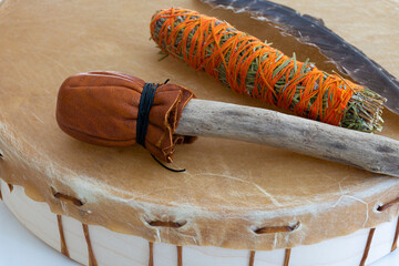 A close up image of a hand made leather meditation drum with smudge stick and sacred feather. 