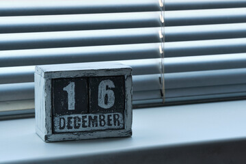 Morning December 16 on wooden calendar standing on window with blinds.
