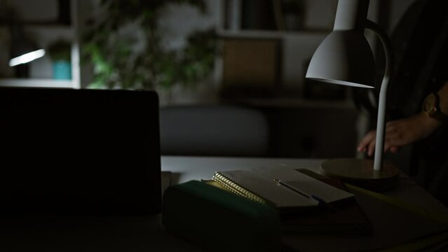 Young caucasian male studying late at night in a home setting with laptop and desk lamp.