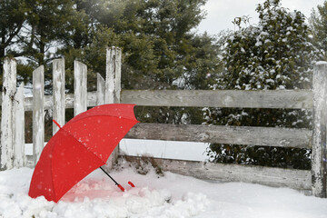 Red umbrella in the snow next to an old wooden fence and gate - winter weather concept background