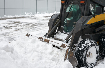 A fragment of a miniature snowplow tractor clearing snow from the adjacent territory after a snow blizzard.