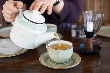 Woman's hands pouring green tea from teapot into cup.