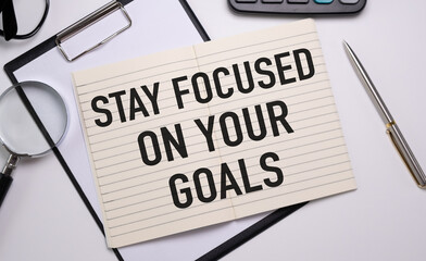 Inspirational quote - Stay focused on your goals. With text message on white paper book, pen, a cup of morning coffee, flower.