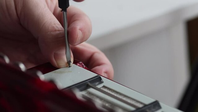 The man fasten with screws the right cover of the button accordion. Bayan repair and maintenance. Close-up.