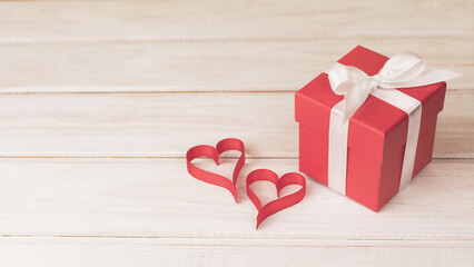 Red gift box and two hearts from ribbon on light wooden surface. Copy space. Valentine's day, wedding, anniversary template. Cute romantic greeting card