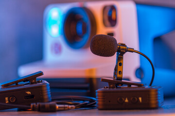 Close up on wireless lavalier microphones, an old fashioned camera is visible in the background, blurred. - 713542487