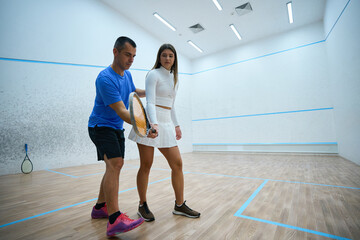 Squash woman player and man coach participate highlighting refined hitting skill
